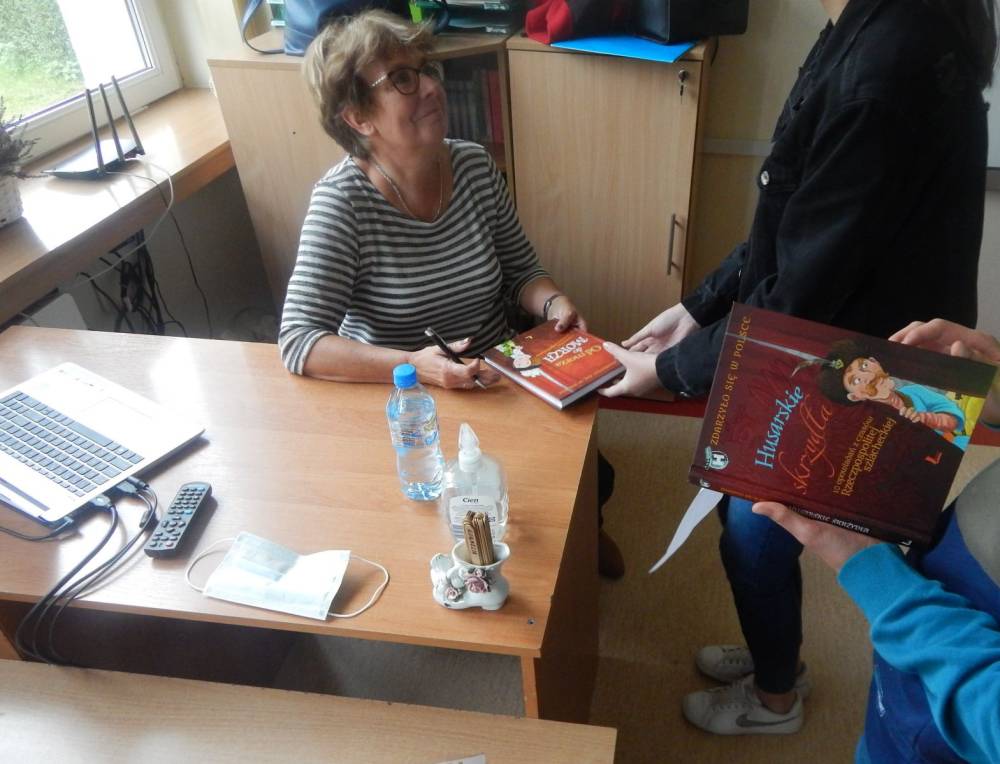 Klasa, Grażyna Bąkieiwcz siedzi przy biurku, podpisuje książkę.