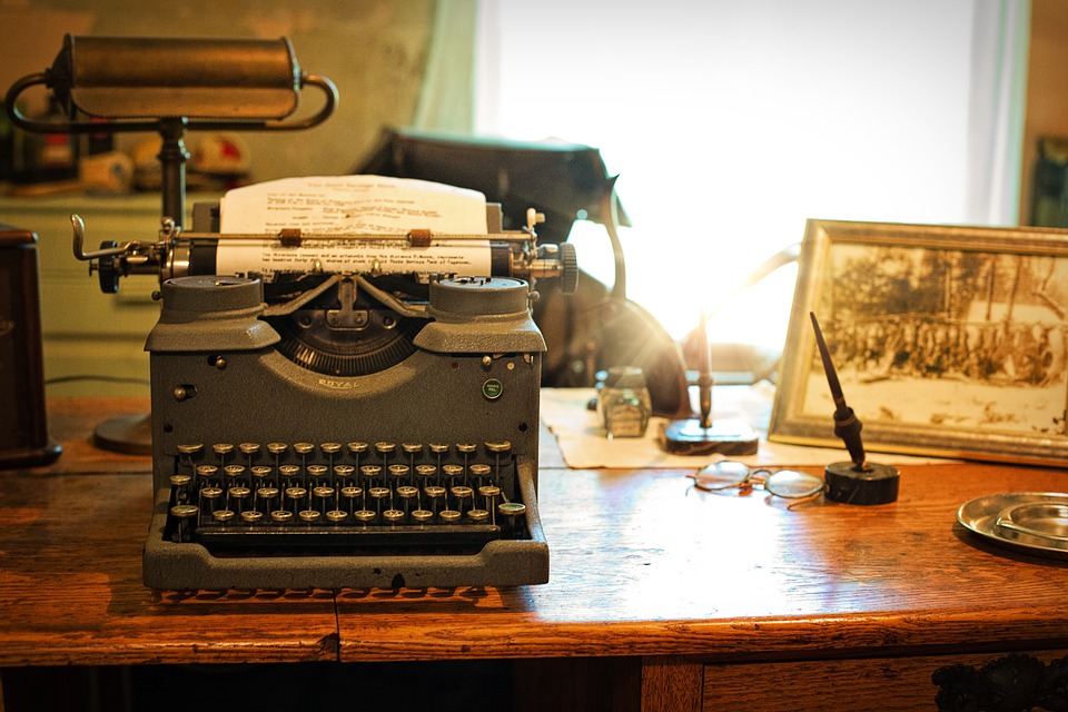 Maszyna do pisania starego typu stojąca na biurku, przeważa kolor brązowy