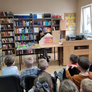 Biblioteka. Dzieci słuchają czytanej przez bibliotekarkę opowieści.