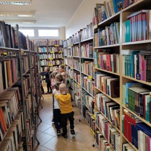 Wnętrze biblioteki, widoczne regały oraz dzieci poruszające się po bibliotece między regałami.