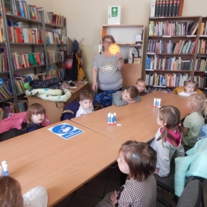 Budynek biblioteki w Szyszyńskich Holendrach, dzieci siedzą przy stołach, oglądają słoneczko, które będą robić.