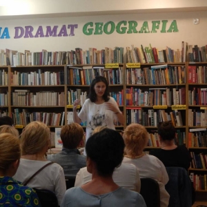 Małgorzata Swędrowska stoi na tle regałów, opowiada bibliotekarkom o swojej pracy.