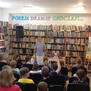 Biblioteka, Eliza Piotrowska stoi, przed nią, na krzesłach ustawionych w rzędy siedzą dzieci